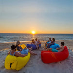 Load image into Gallery viewer, Group of people sitting on colourful inflatable lounger on a beach at sunset.
