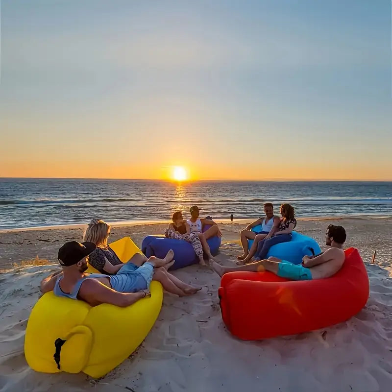 Group of people sitting on colourful inflatable lounger on a beach at sunset.