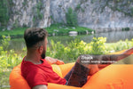 Load image into Gallery viewer, Man sitting on an inflatable lounger by a lake with mountains in the background
