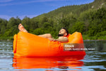 Load image into Gallery viewer, Man lying on an orange inflatable lounger in a lake with greenery in the background

